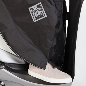 coprigambe da indossare – facile e veloce da mettere tramite tracolla e fasce di regolazione in neoprene sul retro – privo di punti di fissaggio sullo scooter – taglio ergonomico – spacchi laterali per un’ampia libertà di movimento (piede a terra) – costruzione a tre strati: – esterno in tessuto impermeabile – membrana interna impermeabile – imbottitura termica in pile sulle gambe – sistema di ancoraggio al sottosella in caso di parcheggio – pettorina integrata – profilo rifrangente – tasca trasformabile in busta–contenitore di minimo ingombro